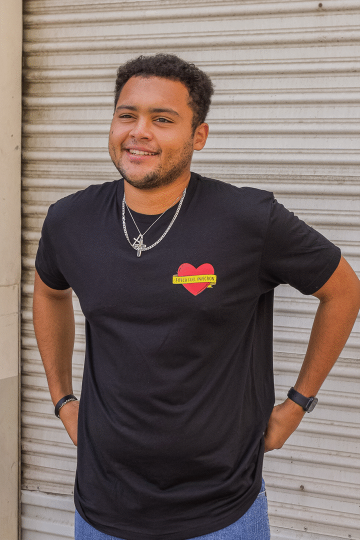 Young man in a black t-shirt with a colorful heart design, smiling outdoors.