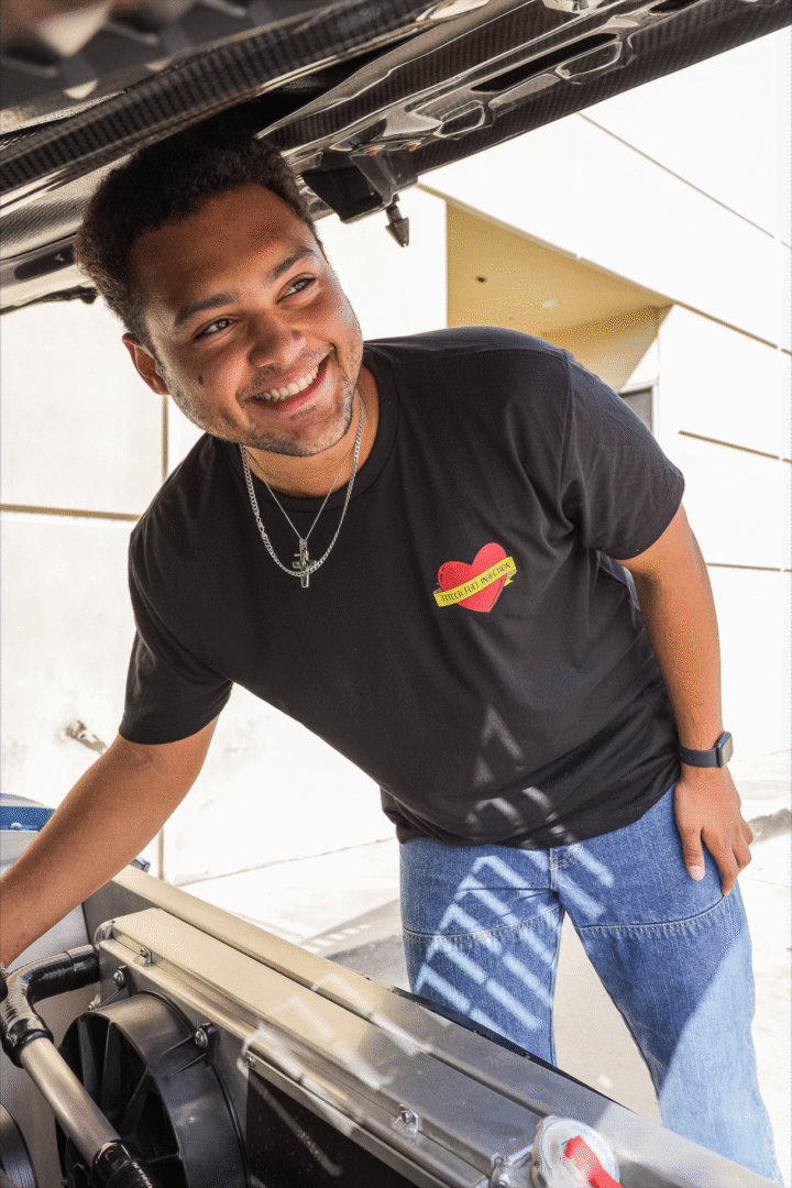Smiling man leaning forward in a casual black t-shirt and striped pants.
