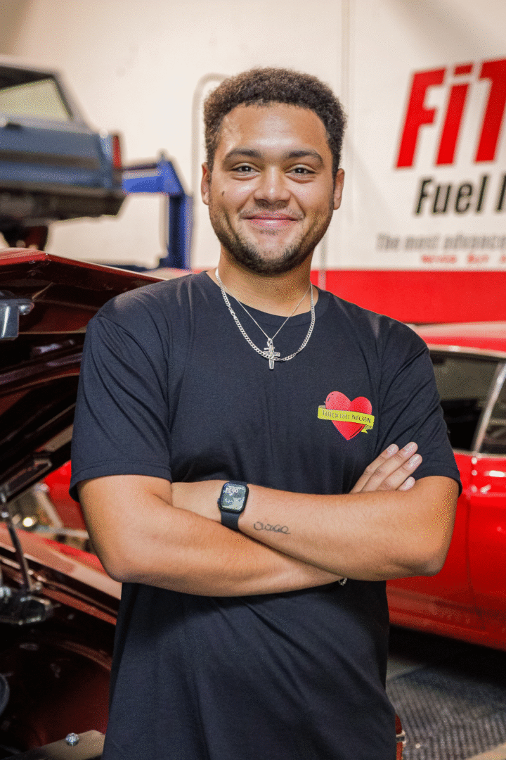 Smiling man with crossed arms standing by a red car in a garage.