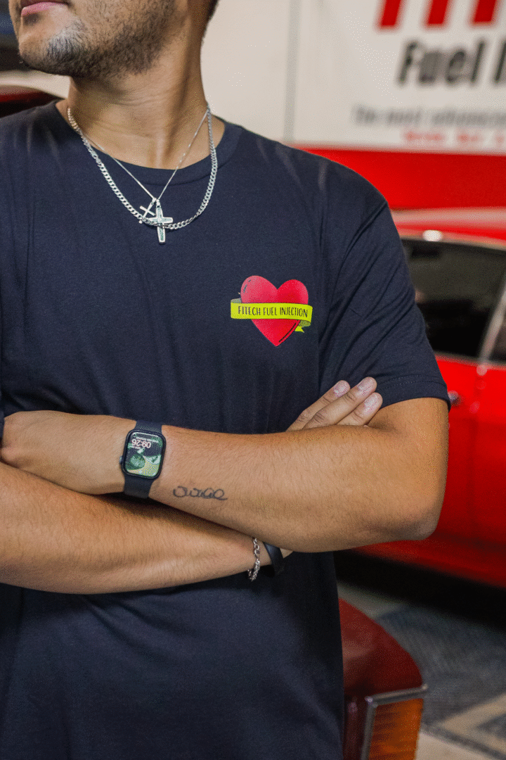 Person wearing a navy shirt with a heart and flames design, crossed arms, and a watch.